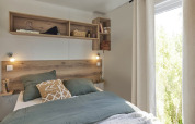 Premium Mobile Home slaapkamer met houten details, groene dekbed, planken en raam bij Provence Vallée.