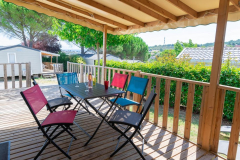 Überdachte Holzterrasse mit bunten Stühlen und Tisch im Premium Mobile Home bei Flower Camping Provence Vallée.