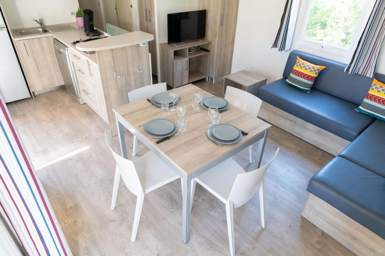 Moderne woonruimte en keuken in Premium Mobile Home met eettafel, bank en kleurrijke kussens.