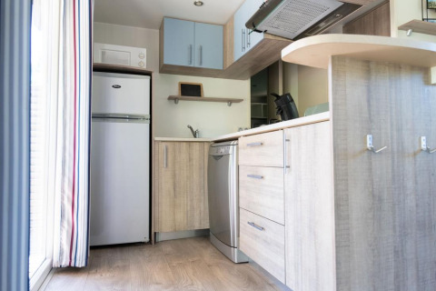 Modern kitchenette with fridge, dishwasher, and wooden cabinets inside a mobile home at Provence Vallée, France.