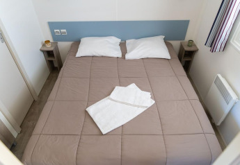 Dormitorio de Premium Mobile Home con cama doble, dos almohadas, toallas y mesitas en Flower Camping Provence Vallée.