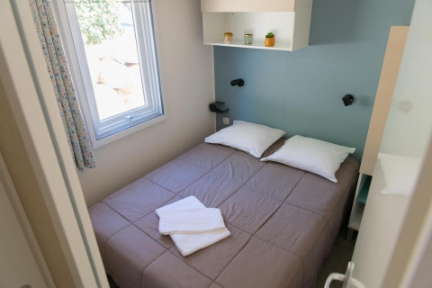Schlafzimmer im Premium Mobile Home mit Doppelbett, Fenster und moderner Einrichtung bei Flower Camping Provence Vallée.