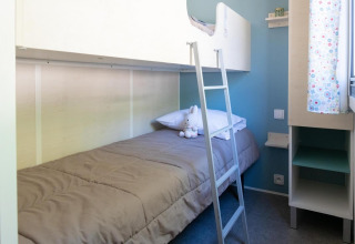Chambre moderne avec lits superposés, linge gris et peluche au Flower Camping Provence Vallée en France.