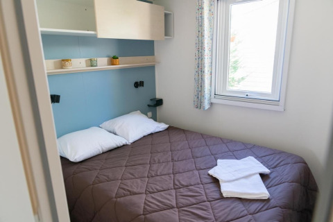 Schlafzimmer mit Doppelbett, zwei Kissen, Fenster und Regal im Premium Mobilheim bei Provence Vallée.