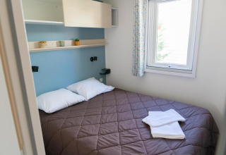 Dormitorio con cama doble, almohadas, ventana y estantes en Mobile Home Premium de Provence Vallée, Francia.