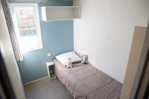 Small bedroom with single bed, plush toys, blue wall, window, and white shelf at Flower Camping Provence Vallée.