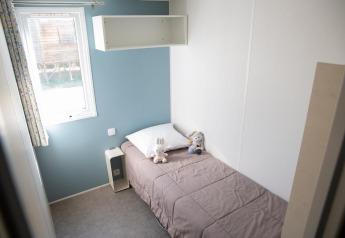 Kleine slaapkamer met enkel bed, knuffels en raam aan Flower Camping Provence Vallée Premium Mobile Home.