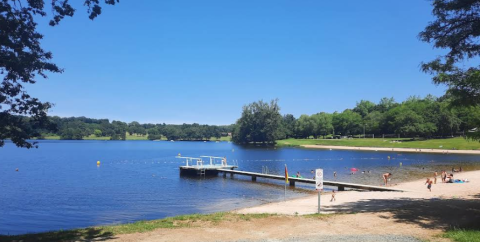 Vista sul lago al Campeggio Seasonova Lac de Bournazel, molo e bagnanti sulla spiaggia in una giornata estiva.