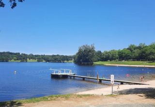 Lake view at Campsite Seasonova Lac de Bournazel, with pier, sandy beach, and people enjoying the summer sun.
