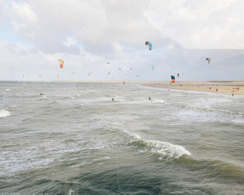 Scorcio costiero vicino a Wolphaartsdijk, Zelanda, Paesi Bassi, con tanti kitesurfer e aquiloni colorati sul mare.