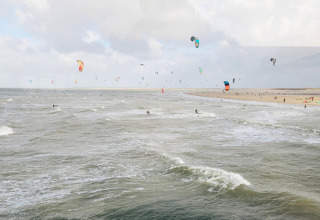 Scorcio costiero vicino a Wolphaartsdijk, Zelanda, Paesi Bassi, con tanti kitesurfer e aquiloni colorati sul mare.