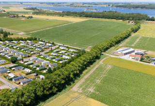 Luftfoto af campingplads de Haas i Zeeland, Holland, med ferieboliger, marker og en flod i baggrunden.