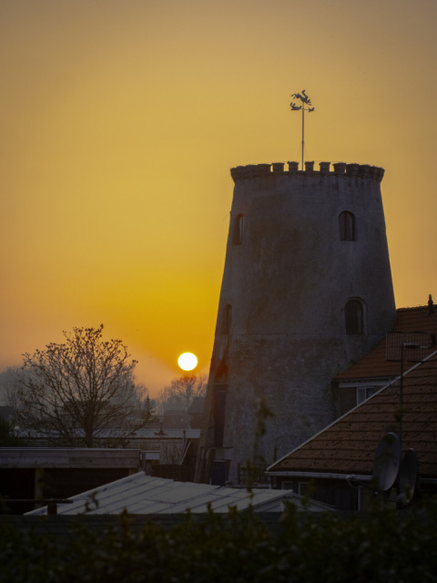 Tramonto dietro una vecchia torre rotonda e tetti a Wolphaartsdijk, Zelanda, Paesi Bassi.