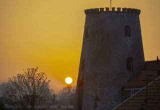 Tramonto dietro una vecchia torre rotonda e tetti a Wolphaartsdijk, Zelanda, Paesi Bassi.