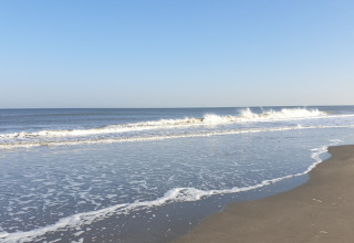 Onde tranquille lambiscono la spiaggia vicino a Wolphaartsdijk, Zelanda, Paesi Bassi, sotto un cielo sereno.