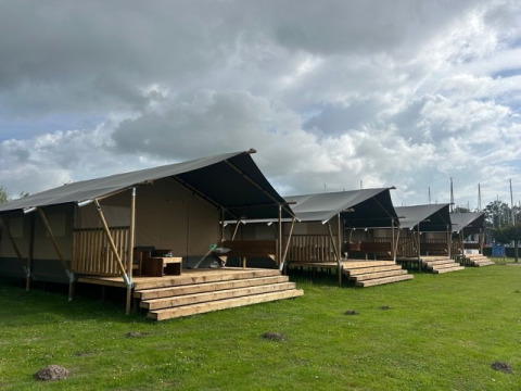 Safari tents with wooden decks at Mini Campsite Marina Warns in the Netherlands under a cloudy sky.