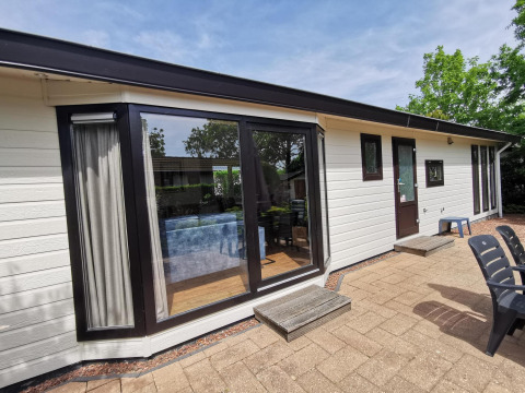 Outdoor photo of a modern cabin named Comfort featuring large glass windows, patio, and outdoor chairs in sun.