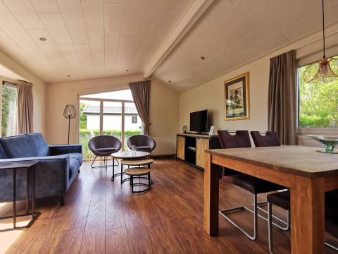 Modern living room inside the Comfort cabin at De Woudhoeve in the Netherlands, featuring large windows and wood furniture.