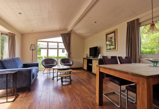 Modern living room inside the Comfort cabin at De Woudhoeve in the Netherlands, featuring large windows and wood furniture.