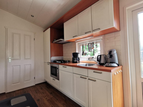 Modern kitchen in the ‘Comfort’ cabin at De Woudhoeve, Netherlands, featuring white cabinets and appliances.