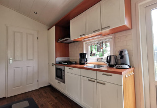 Modern kitchen in the ‘Comfort’ cabin at De Woudhoeve, Netherlands, featuring white cabinets and appliances.