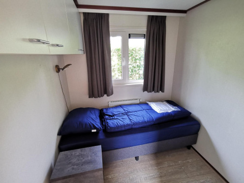 Small bedroom inside the 'Comfort' cabin at De Woudhoeve, Netherlands, featuring a single bed and window.