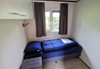 Small bedroom inside the 'Comfort' cabin at De Woudhoeve, Netherlands, featuring a single bed and window.