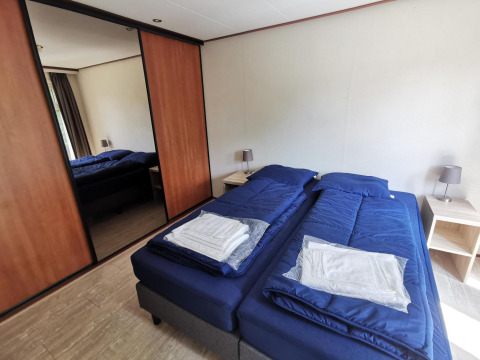Bedroom in Comfort cabin at De Woudhoeve, Netherlands, with twin beds and blue bedding and nightstands.