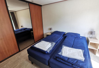 Bedroom in Comfort cabin at De Woudhoeve, Netherlands, with twin beds and blue bedding and nightstands.