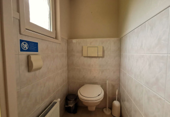 Et badeværelse med væghængt toilet, toiletbørste, skraldespand og vindue i hytten 'Comfort'.