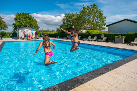 Two children jump into an outdoor pool at a Comfort cabin complex in De Woudhoeve, Netherlands.