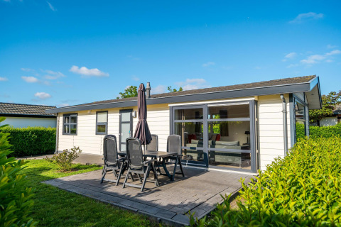 Outdoor photo of Comfort cabin featuring patio, garden furniture, and lush greenery under blue sky.