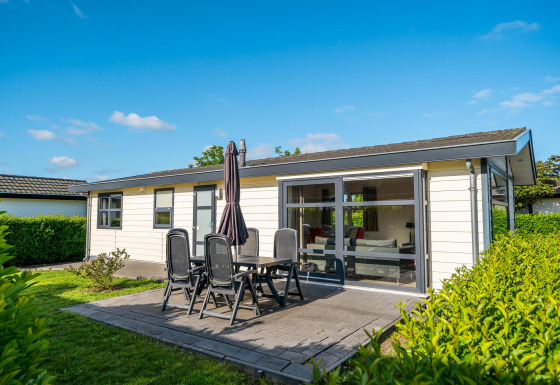 Outdoor photo of Comfort cabin featuring patio, garden furniture, and lush greenery under blue sky.