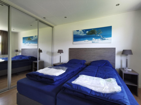 Bedroom in a Comfort cabin at De Woudhoeve, Netherlands, featuring twin beds with blue bedding and mirror.