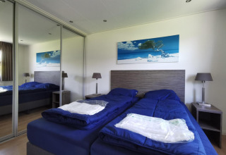 Bedroom in a Comfort cabin at De Woudhoeve, Netherlands, featuring twin beds with blue bedding and mirror.