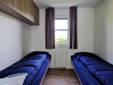 Simple twin room in the 'Comfort' cabin at De Woudhoeve, Netherlands, with blue bedding and a window.
