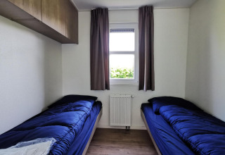 Simple twin room in the 'Comfort' cabin at De Woudhoeve, Netherlands, with blue bedding and a window.