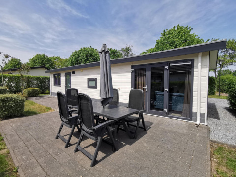 Outdoor patio with six chairs and umbrella in front of a modern Comfort cabin at De Woudhoeve, Netherlands.