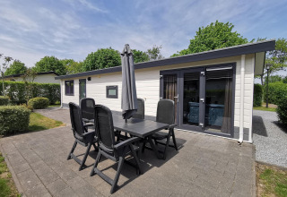 Outdoor patio with six chairs and umbrella in front of a modern Comfort cabin at De Woudhoeve, Netherlands.
