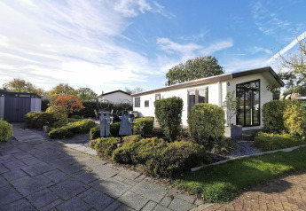 Moderne hytte Comfort med velplejet have, stor terrasse og havehus under en klar himmel.