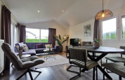 Modernes Wohnzimmer in der „Comfort“-Hütte in De Woudhoeve, Niederlande, mit Essbereich und großen Fenstern.