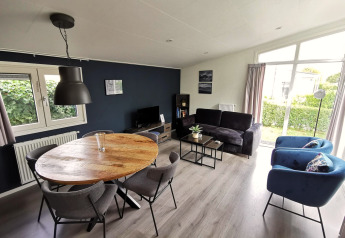 Moderne woonkamer in de ‘Comfort’ chalet bij De Woudhoeve, Nederland, met zetel, eettafel en grote ramen.