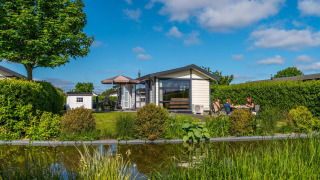 Comfort vakantiewoning bij De Woudhoeve, Nederland, met terras, vijver en mensen in de tuin.