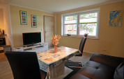 Living area of Am Strand lodge in Germany with dining table, sofa, TV, large windows, and decor.