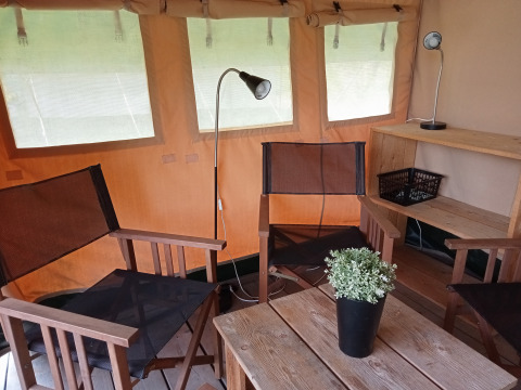 Interno di una tenda safari presso il Campeggio La Perle in Francia con sedie, lampade e pianta.