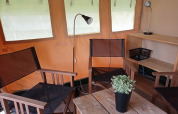 Intérieur d'une tente safari au Camping La Perle en France avec des chaises, lampes et une plante verte.
