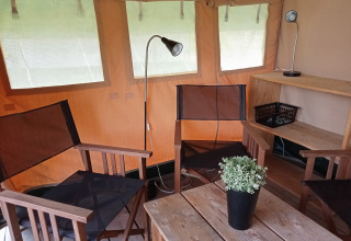 Intérieur d'une tente safari au Camping La Perle en France avec des chaises, lampes et une plante verte.