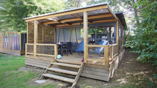Træhytte ved Cottage Morea med overdækket terrasse, havemøbler og omgivet af grønne træer og buske.