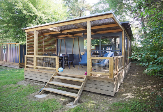 Træhytte ved Cottage Morea med overdækket terrasse, havemøbler og omgivet af grønne træer og buske.