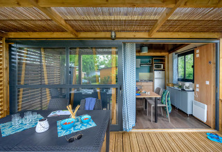 Udendørs terrasse og interiør i Cottage «Morea» ved Campsite Le Château, Frankrig med spisebord og køkken.